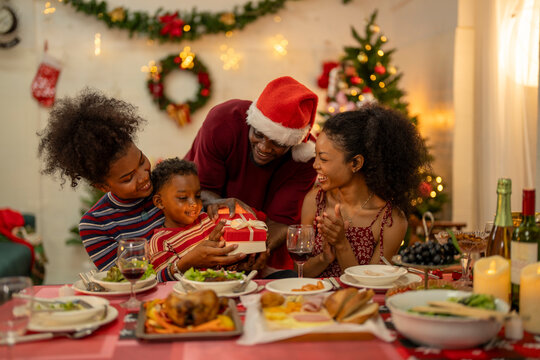 An African American family gathers for a festive Christmas party, enjoying snacks, drinks, and laughter in their decorated living room. Concept for holiday entertaining and joyful feasts. - Powered by Adobe