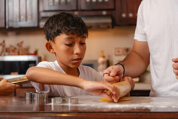 Boy learning to roll cookie dough with father in cozy kitchen