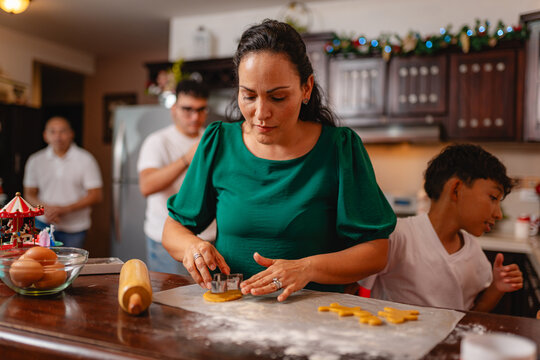 Woman cutting Christmas cookies in festive kitchen with family - Powered by Adobe