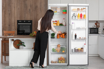 Beautiful businesswoman taking food from open fridge in kitchen, back view © Pixel-Shot