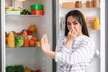 Beautiful woman feeling bad smell from open fridge in kitchen