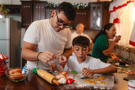 Latino teen and young man decorating Christmas cookies in festive kitchen