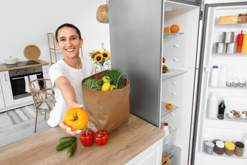 Young woman with bag of food near open fridge in kitchen