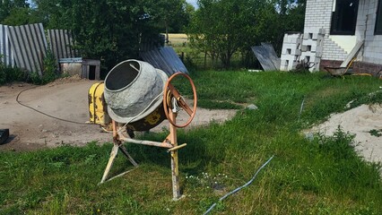 Construction concrete cement mixer equipment stands idle beside a building site in a rural area...