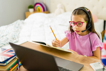 Little girl learning english online with a laptop and headphones at home