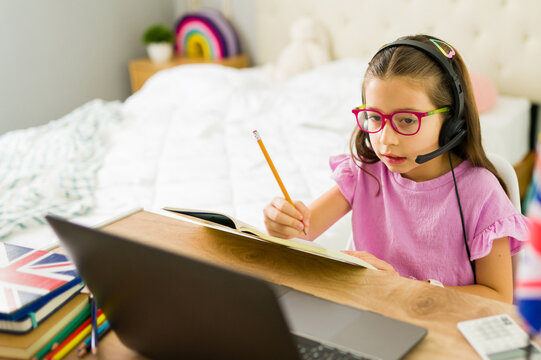 Little girl learning english online with a laptop and headphones at home - Powered by Adobe