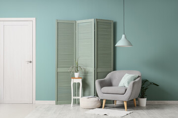 Interior of living room with grey armchair, green folding screen and table