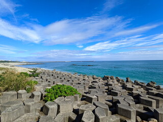 A beach half-filled with tetrapod and sandy at the other side facing the Pacific Ocean with a lighthouse in sight under a sunny blue sky during the pandemic