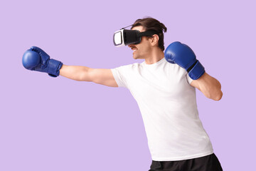 Sporty young man in VR glasses with boxing gloves on lilac background