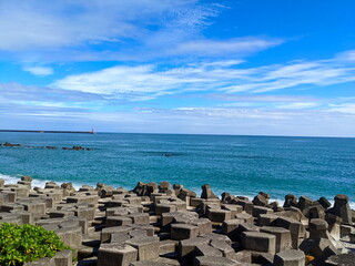 A beach filled with tetrapod facing the Pacific Ocean with a lighthouse in sight under a sunny blue sky during the pandemic
