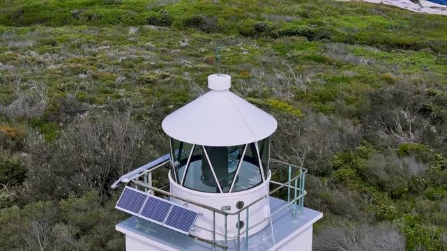 Kurnell, Sydney, Australia: Drone Video: Flying in a circle above Cape Baily Lighthouse -close up view of the top with solar panels and a black bird standing on the rail.