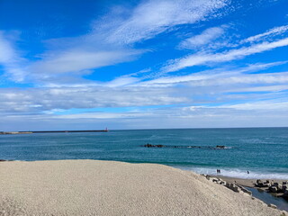 Jian Stream leading to the Pacific Ocean via a beach with tetrapods and people enjoying the beach under a sunny blue sky during the pandemic with a lighthouse in sight