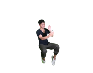 A young man in casual attire is captured mid-air in a squatting pose, looking down at his hands against a white background.