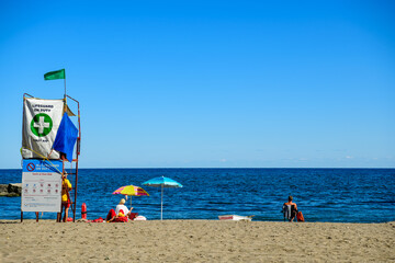 lifeguard chair and sun umbrellas on beach in summer with people, blue sky, and blue water shot on...