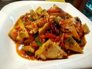 Spicy stir-fried tofu with bell peppers and chili sauce – Asian plant-based dish on white plat