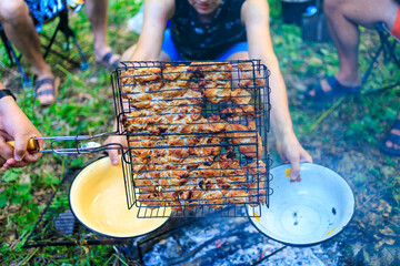 A man is cooking food on a grill while another man holds a bowl of food