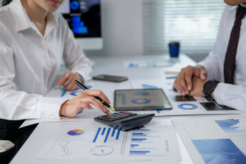 Two people are sitting at a table with a calculator and a bunch of papers