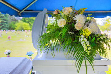 Beautiful arrangement of flowers adorns casket at an outdoor burial ceremony in tranquil cemetery.