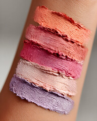 Eyeshadow swatches in coral, peach, pink, and lavender tones across arm