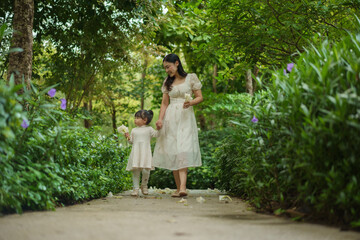 happy mother and toddler girl in white dress walking in flower garden
