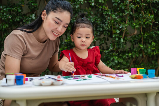 happy mother and toddler girl painting watercolor in paper at backyard.