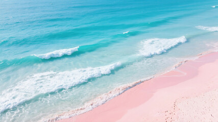 Aerial drone view of a stunning and exotic pink sand beach with gentle turquoise ocean waves