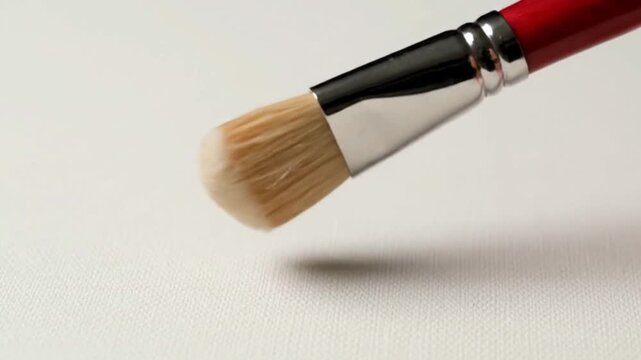 A makeup brush with a red handle rests on textured white surface