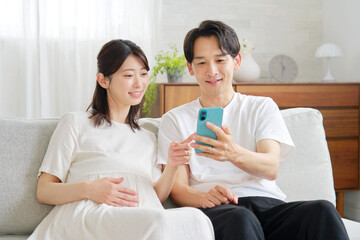 リビングでスマホを使う妊娠中の妻と夫