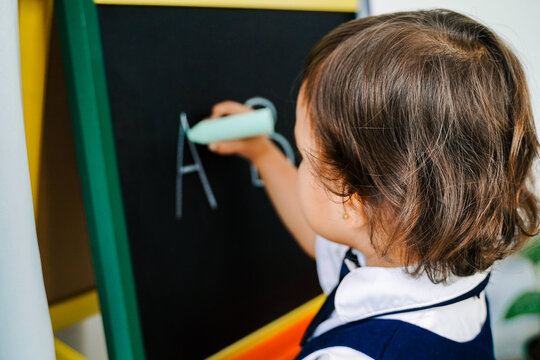 Toddler girl learning to write on chalkboard – Early childhood education and learning development concept