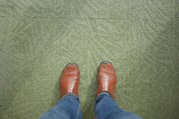 Brown shoes on green carpet while standing indoors