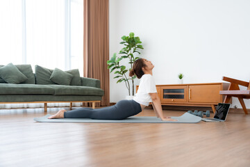 Young Asian woman stretching yoga workout on exercise mat while online training class with computer...