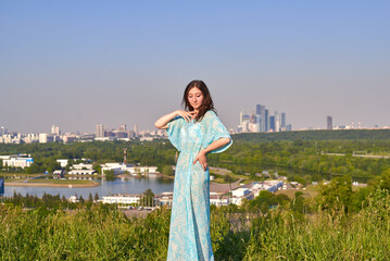 A woman in a navy blue dress is standing on a hill with a panoramic view of the city below. The sky...