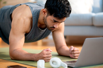 Young asian man doing plank exercise in living room at home while watching online workout tutorial...