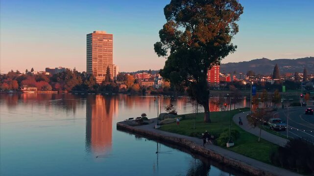 Lake Merritt in Oakland, California, USA, at sunset. People are walking and jogging along the lake's edge, enjoying the scenery and the fresh air.