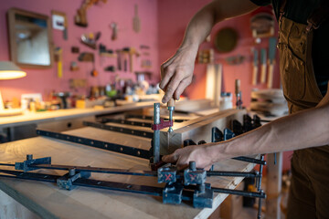 Carpenter hands tighten clamps with screwdriver to bind glued beams for large wooden board for...