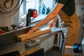 Woodworker hands work on electric planer saw, trimming wood pieces. Excess cutting, surface...