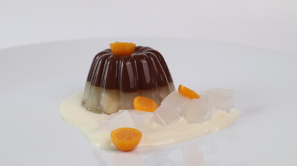 chocolate coconut pudding on a white plate with small orange fruit topping