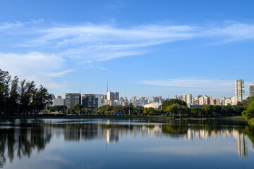 Obraz premium Vista do skyline de São Paulo refletido no lago do Parque Ibirapuera em um dia claro, destacando a harmonia entre natureza e urbanismo sob um céu azul.