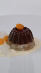 chocolate coconut pudding on a white plate with small orange fruit topping