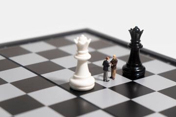Miniature people shaking hands among chess pieces. concept of cooperation and business agreement.