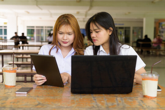 Young Thai University Students Relaxing Together at Campus Cafe Outdoors Using Technology - Powered by Adobe