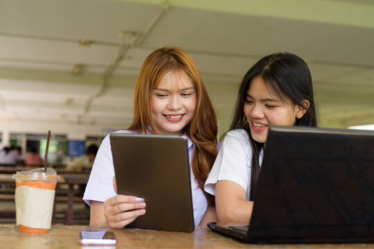 Young Thai University Students Relaxing Together at Campus Cafe Outdoors Using Technology - Powered by Adobe