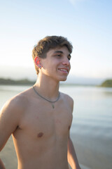 Jovem à beira-mar durante o pôr do sol, com expressão tranquila e look casual, representando...