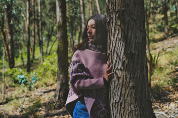Fashion model wearing poncho leaning against tree in forest