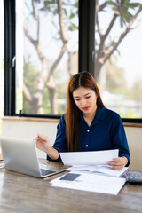 Thoughtful asian female sit at home workplace hold financial documents look on laptop screen check...