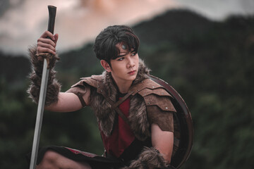 Young warrior with sword and shield in wilderness, dramatic pose