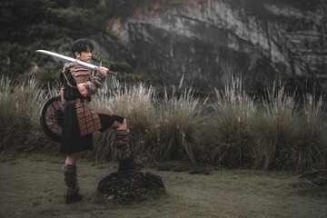 Warrior in Armor Posing with Sword and Shield in Natural Landscape