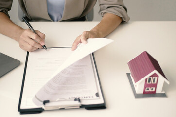 A young woman real estate service worker is sitting at a computer searching for information and...