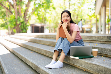 Asian college student sitting on the stairs of a university campus, reading a book and studying....
