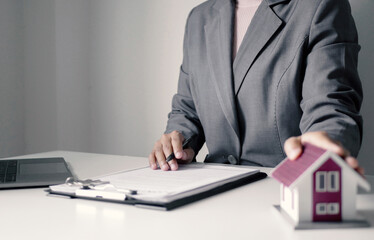 A young woman real estate service worker is sitting at a computer searching for information and...